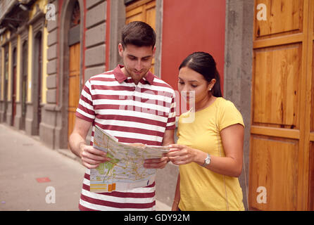 Young couple studying a map while smiling happily and dressed casually in t-shirts with old buildings behind them Stock Photo