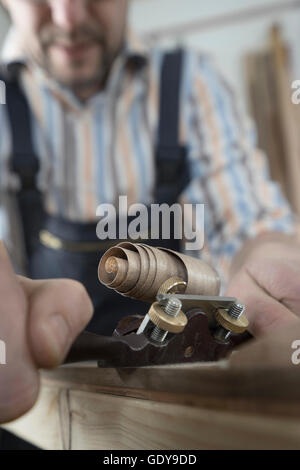 Male bow maker shaving wood and giving it a shape of bow in workshop, Bavaria, Germany Stock Photo