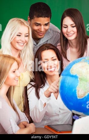 Geography teacher showing something on the globe to her students. Stock Photo