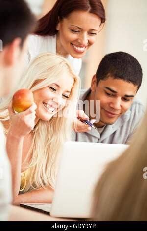 Smiling teacher showing something to her students on a laptop. Stock Photo