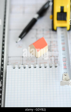 Architecture plans of a building with Small model house on top of blueprints, pen, ruler and notebook Stock Photo