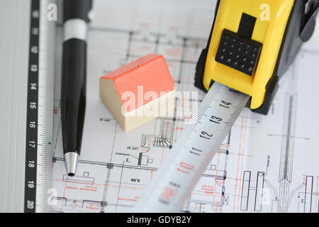 Architecture plans of a building with Small model house on top of blueprints, pen and ruler Stock Photo
