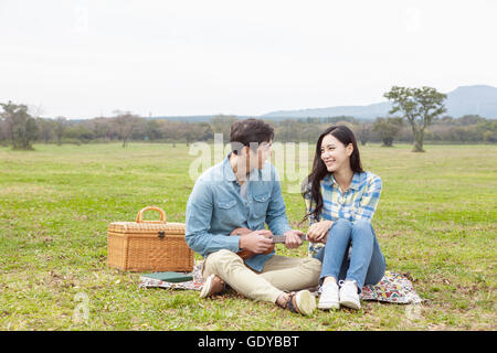 Young smiling couple playing a ukulele sitting face to face sitting on grassland during picnic Stock Photo