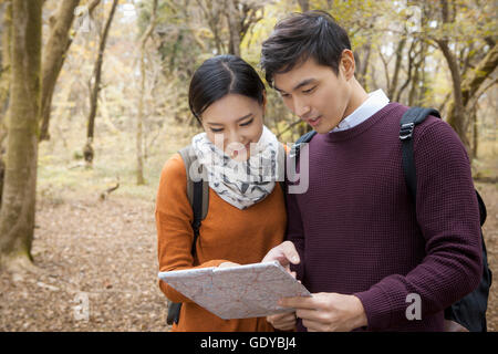 Portrait of young smiling couple trekkers reading a map in forest Stock Photo