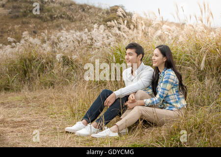 Side view of young smiling couple sitting and resting on silver grass field Stock Photo