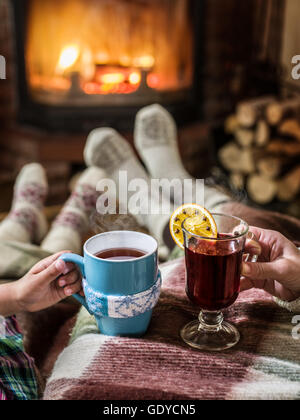 Warming and relaxing near fireplace. Woman feet near the cup of hot drink in front of fire. Stock Photo