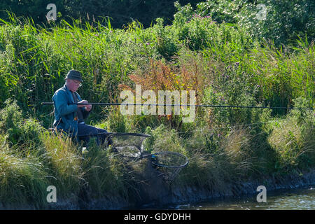 A man sat on the banks of a canal in the Norfolk Broads Stock Photo