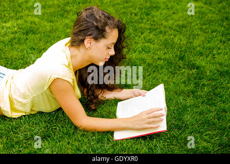 Beautiful young woman lying on the grass and reading a book Stock Photo