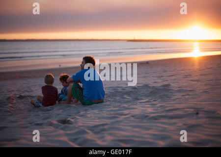 Father with two kids sitting on beach during sunset, Viana do Castelo, Norte Region, Portugal