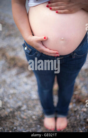 Pregnant woman standing with hands on stomach at stone beach, Ammersee, Upper Bavaria, Bavaria, Germany Stock Photo