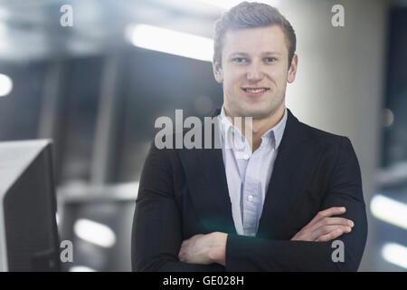 Young businessman standing with arms crossed and working till late in office, Freiburg im Breisgau, Baden-Württemberg, Germany Stock Photo