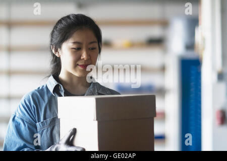 Young female engineer holding cardboard box in an industrial plant, Freiburg im Breisgau, Baden-Württemberg, Germany Stock Photo