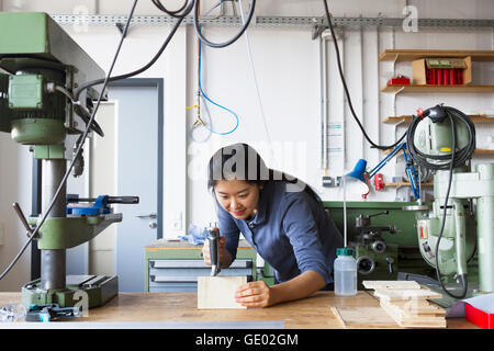 Young female carpenter sawing a piece of wood in an industrial plant, Freiburg im Breisgau, Baden-Württemberg, Germany Stock Photo