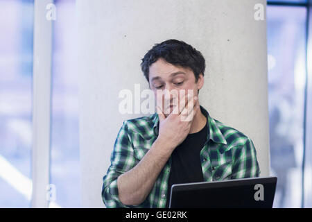 Mid adult man using laptop in the office and thinking, Freiburg im Breisgau, Baden-Württemberg, Germany Stock Photo