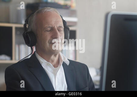 Senior businessman listening to music with headphones in the office, Freiburg im Breisgau, Baden-Württemberg, Germany Stock Photo