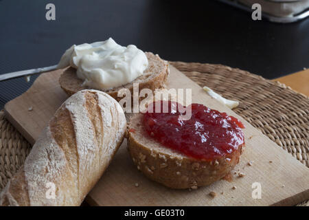Baguette, cream cheese, marmalade, bun on chopping board Stock Photo