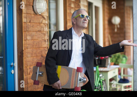 Senior businessman wearing suit and holding longboarding, Freiburg im Breisgau, Baden-Württemberg, Germany Stock Photo
