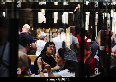 People sitting in a restaurant in Covent Garden and, in background, standing watching a street entertainer balancing on a ladder Stock Photo