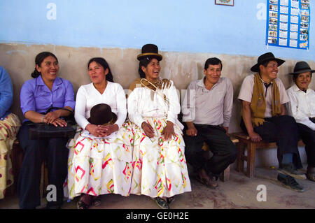 Bolivian men and women laughing and smiling in a village hall, wearing traditional indigenous clothing and bowler hats Stock Photo