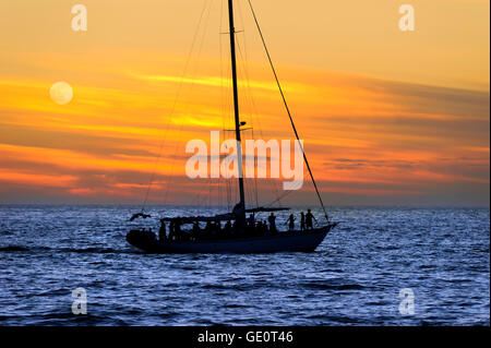 A sailboat full of people saiiing and having fun at sunset on the ocean. Stock Photo