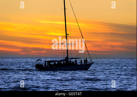Silhouette of a  sailboat full of people sailing and having fun at sunset on the ocean. Stock Photo
