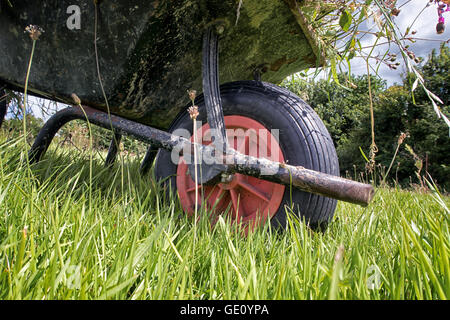 A full garden wheel barrow on long grass. Taken from a low view point showing the wheel. Stock Photo