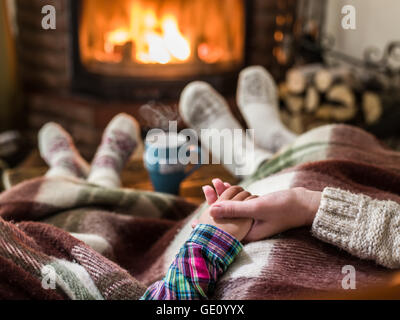 Warming and relaxing near fireplace. Mother and daughter holding hands in front of fire. Stock Photo