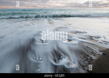 Pebbles on the beach on a black sand and flowing sea water creating nice textures. Long exposure image. Stock Photo