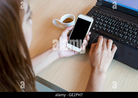 Woman using a touch screen of white smartphone with black notebook or laptop on the wooden table and hand holding aromatic Stock Photo