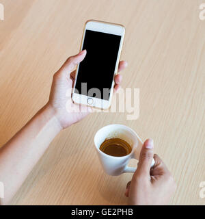 Hand using a touch screen of white smartphone on the wooden table and hand holding aromatic cappuccino, white coffee cup, close Stock Photo