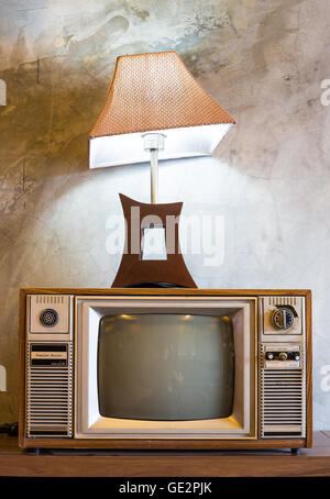 retro tv with wooden case and lantern in room with vintage wallpaper on wood table Stock Photo