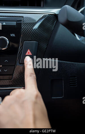 Closeup of young woman pressing emergency button on car sport dashboard. Stock Photo