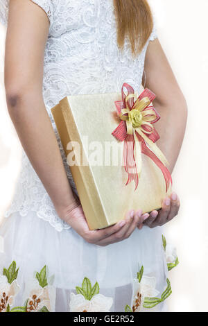 Women in white hiding a gift behind her back. Stock Photo