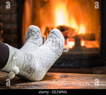 Warming and relaxing near fireplace. Woman feet near in front of fire. Stock Photo