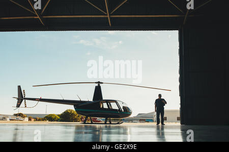 Full length image of pilot with a helicopter in an airplane hangar. Stock Photo