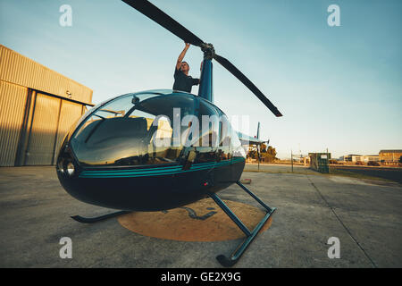 Image of pilot checking the helicopter rotor blades at the airfield. Man inspecting his aircraft before a flight. Stock Photo