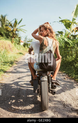 Rear view shot of young couple riding motorcycle on rural road. Attractive young female sitting on back of her boyfriend riding Stock Photo