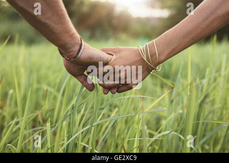 Close up shot of man and woman holding hands in grass field. Young couple in love with hand in hand. Stock Photo