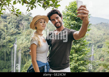 Loving young couple taking self portrait with waterfall in background. Man and woman on vacation in forest taking selfie with th Stock Photo