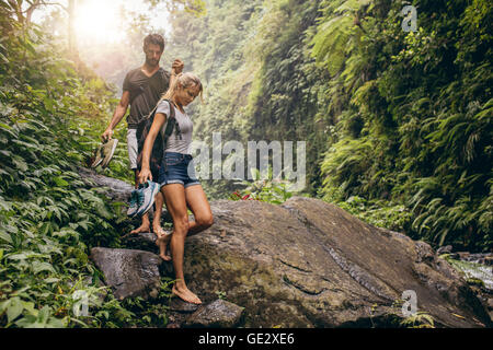 Shot of young couple walking through the mountain trail. Man and woman hiking on mountain trail barefoot. Stock Photo