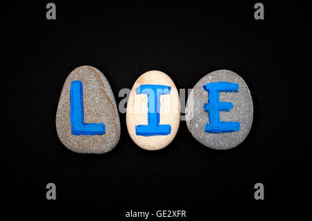 Word Lie spell out from stones with blue letters on black background. Letters drawn by me Stock Photo