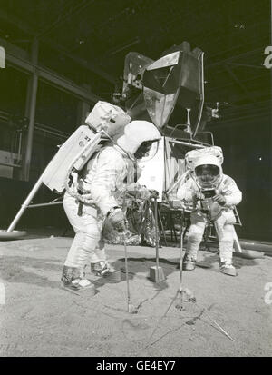The Apollo 11 crew simulates deploying and using lunar tools on the surface of the Moon during a training exercise on April 22, 1969. Astronaut Buzz (Aldrin Jr. on left), lunar module pilot, uses a scoop and tongs to pick up a soil sample. Astronaut Neil A. Armstrong, Apollo 11 commander, holds a bag to receive the sample. In the background is a Lunar Module mockup.  Image # : S-69-32233  Date: April 22, 1969 Stock Photo