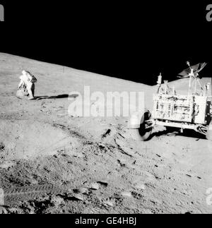 Astronaut David R. Scott, mission commander, with tongs and gnomon in hand, studies a boulder on the slope of Hadley Delta during the Apollo 15 lunar surface extravehicular activity. The Lunar Roving Vehicle (LRV) or Rover is in right foreground. View is looking slightly south of west. &quot;Bennett Hill&quot; is at extreme right. Astronaut James B. Irwin, lunar module pilot, took this photograph.   Image # : AS15-85-11437 Date: August 1, 1971 Stock Photo