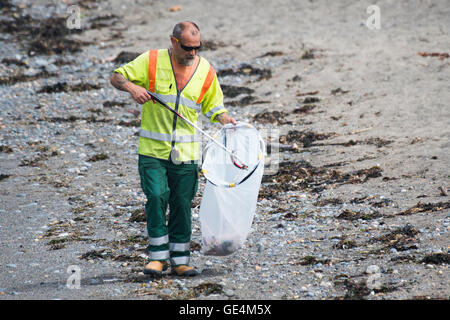 A man, employed by Ceredigion County Council local authority,  working as a litter picker cleaning rubbish trash plastic waste off the the beach in Aberystwyth Wales UK Stock Photo
