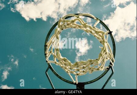 Abstract perspective of a netball rim with net against a blue sky and cloud background. Stock Photo