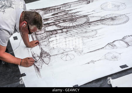 Street artist making fine detailed black and white drawing of imaginary machines on paper lying on the ground Stock Photo