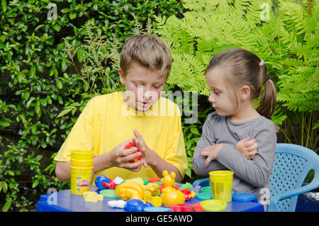 Three year old girl and ten-year-old boy, brother and sister, playing with Play-Doh modeling putty. UK. Outside in garden. Stock Photo