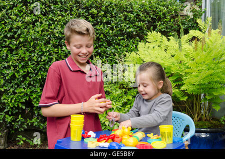 Three year old girl and ten-year-old boy, brother and sister, playing with Play-Doh modeling putty. UK. Outside in garden. Stock Photo