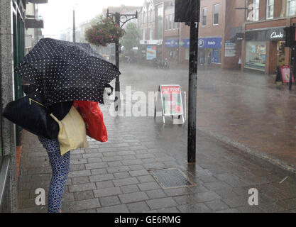 A woman trying to shelter herself and her shopping bags from torrential rain with a small umbrella in the town of Newbury, Berkshire, UK Stock Photo