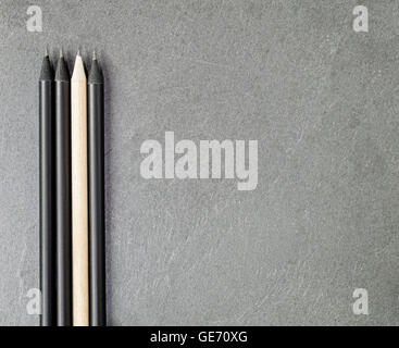 Light colored pencil among three black ones on a gray granite slate. Stock Photo